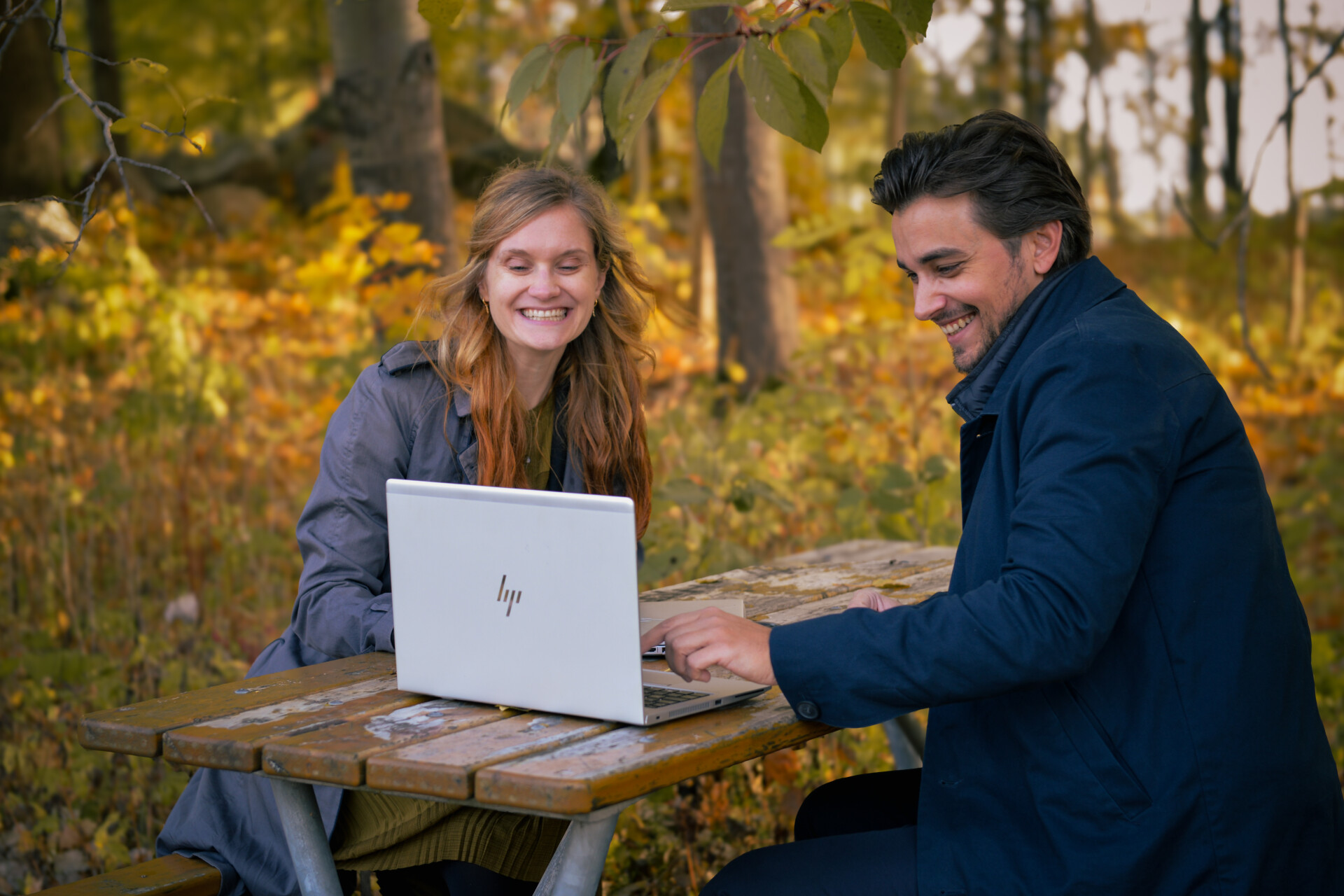 En kvinna och em man är glada och tittar på en begagnad laptop i naturmiljö.